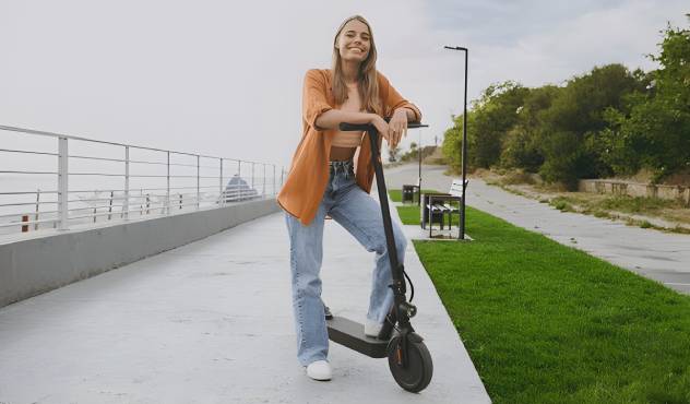 A képen egy lány áll és mutatja az elektromos rollerjét